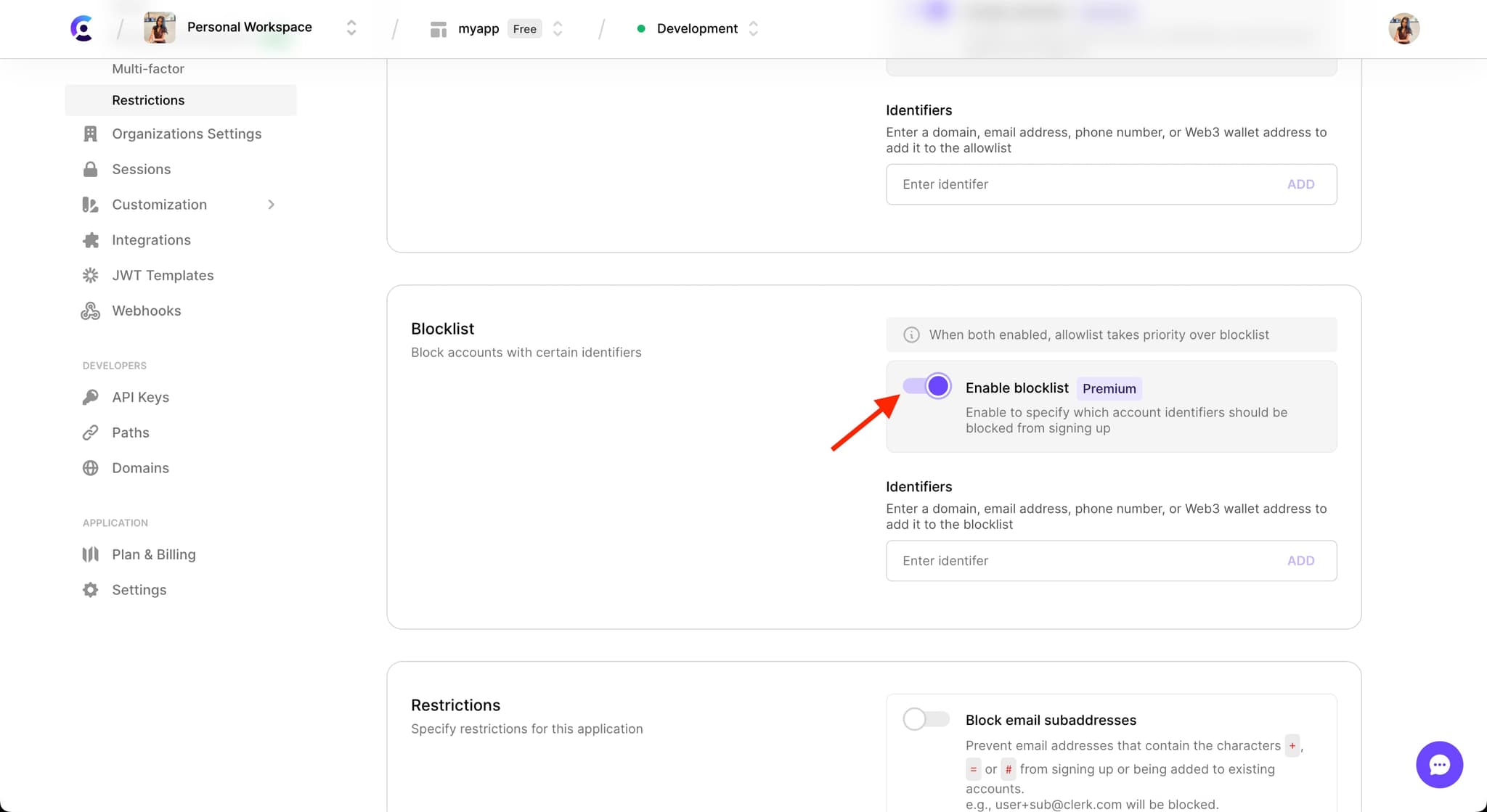 The 'Blocklist' section in the 'Restrictions' tab under the 'User & Authentication' section of the Clerk Dashboard. A red arrow is pointing to the 'Enable blocklist' toggle, which is toggled on.